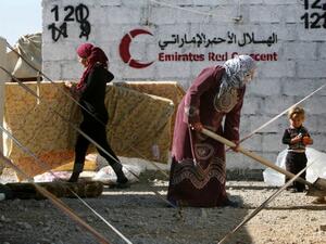 Syrian-Kurdish refugees work near tents erected by the United Arab Emirate's Red Crescent as aid is distributed at the Qushtapa refugee camp, 15 kilometers South of Arbil. [AFP]