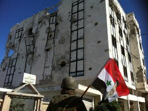 A Syrian army's soldier a national flag featuring Syria's President Bashar Assad in front of a building left in ruins with on Wednesday in Qusayr. AFP Photo