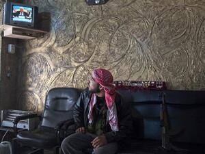 A rebel soldier watches the satellite TV news, waiting to learn his country's fate