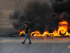 LEBANON, Tripoli : A youth walks past burning tires across a street in the northern city of Tripoli, on June 23, 2013, during protests in support of Sunni Muslim Sheikh Ahmad al-Assir whose supporters have clashed with the Lebanese army in the southern Lebanese city of Sidon. (Credit: AFP)