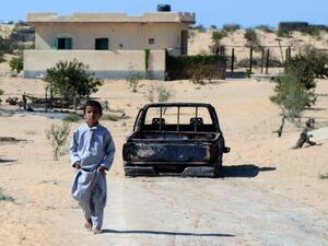 An Egyptian child walks in front of the wreckage of a burnt down car, the day after an attack by Egyptian Army in a village on the outskirt of the Northern Sinai (AFP)
