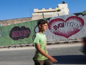  A Syrian boy walks past graffiti in the village of Kfar Nubul in the northwestern province of Idlib on Monday. (AFP)