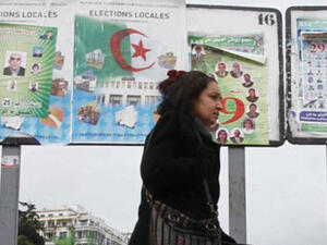 امراة تمر من امام ملصقات انتخابية في الجزائر
