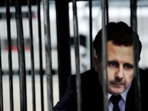 متظاهر يضع قناعا يمثل الرئيس السوري بشار الاسد ويجلس ارضا في قفص امام المحكمة الجنائية الدولية في لاهاي
