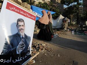 Women walk past a poster of deposed president Mohamed Morsi on July 25 in Cairo.  (AFP / FAYEZ NURELDINE)