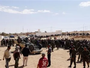 جنود من الجيش التونسي وسكان ولاجئين ليبيين بالقرب من سيارة مقلوبة تابعة للقوات القذافي بالقرب من الذهيبة 
