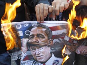 A protester holds a poster burning on which is depicted former US president George W. Bush taking off a mask of current President Barack Obama during a demonstration of in Beirut. (AFP)
