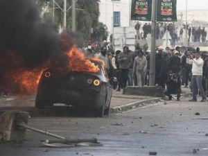محتجون يشاهدون سيارة تحترق خلال اشتباكات مع الشرطة قرب المقبرة الذي دفن بها المعارض شكري بلعيد بتونس العاصمة يوم الجمعة
