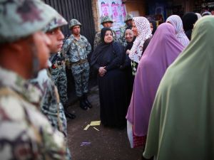 Women standing near The Citadel wait in line to vote watched by soldiers.