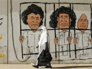 امراة تمر أمام رسم على جدار للزعيم الليبي الراحل معمر القذافي وابنه سيف ورئيس مخابراته عبدالله السنوسي في طرابلس 
