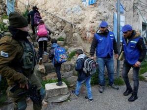 جندي إسرائيلي (يسار) يراقب نشطاء مجموعة "شبان ضد الاستيطان" الفلسطينية وهم يرافقون أطفالا في طريقهم لمدارسهم في مدينة الخليل في الضفة الغربية
