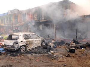 The wreckage of a burnt vehicle remains in front of burning shops following a bomb blast in central Nigeria (AFP/File)