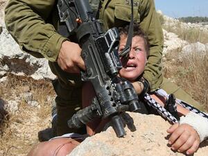 An Israeli soldier forcefully holds down eleven-year-old Mohammed Tamimi, his left arm in a cast, during clashes in the West Bank village of Nabi Saleh, August 28, 2015. (AFP/Abbas Momani)