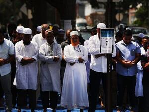 A sketch of a suspect is secured to a post as men pray outside of the Al-Furqan Jame Masjid mosque where Imam Maulama Akonjee and his assistant, Thara Uddin, 64, were killed in a shooting on August 13 in the Queens borough of New York on August 15, 2016. (AFP/Getty Images/Spencer Platt)
