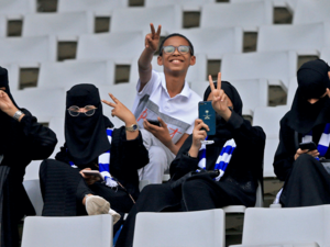 مشجعو كرة القدم السعوديون ، بمن فيهم النساء ، يبثون لفتة النصر وهم ينتظرون فريقهم في المدرجات قبيل مباراة كرة القدم الفاصلة في دوري أبطال آسيا بين الأهلي السعودي والهلال على ملعب جامعة الملك سعود بالعاصمة السعودية الرياض في 13 أغسطس 2019.