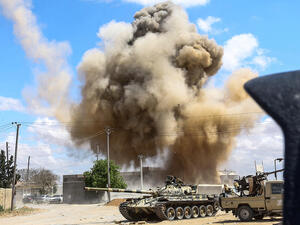 This picture taken on April 12, 2019 shows a smoke plume rising from an air strike behind a tank and technicals belonging to forces loyal to Libya's Government of National Accord. (Mahmud TURKIA / AFP)