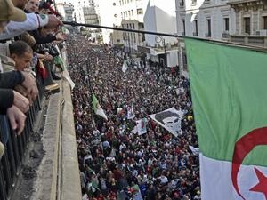Algerians wave a national flag from a balcony as they watch anti-government demonstrators march in the capital Algiers on December 6, 2019, ahead of the presidential vote scheduled for December 12.  (AFP/ File Photo)