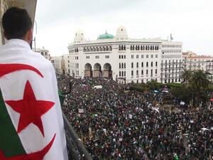 An Algerian man draped in a national flag watches as protesters gather for a demonstration against ailing President Abdelaziz Bouteflika in front of La Grande Poste. (AFP)