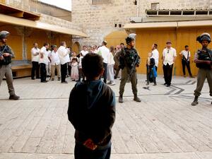 A Palestinian child looks at Israeli soldiers standing guard as settlers stroll through the market in the divided West Bank town of Hebron, on April 13, 2019. (HAZEM BADER / AFP)