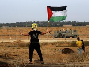 A Palestinian protester wearing a mask waves a national flag during a demonstration near the border with Israel, east of Khan Yunis in the southern Gaza Strip, on April 26, 2019.  (Said KHATIB / AFP)