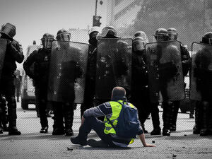 A Yellow Vest protester sits in front of police (AFP/FILE edited by Rami Khoury/Al Bawaba) banner image