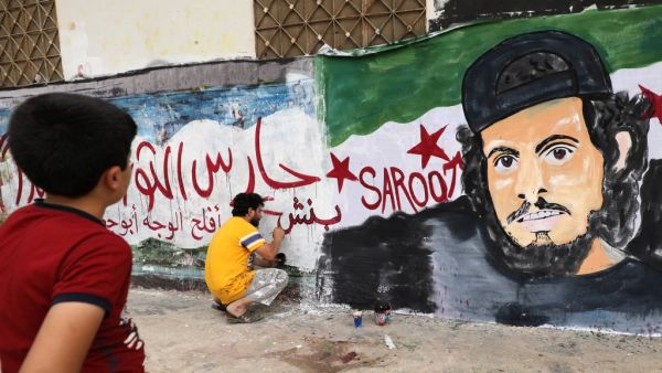 A child watches as a local artist works on a mural painting showing the late Syrian rebel fighter Abdel-Basset al-Sarout in the town of Binnish in the jihadist-held northern Idlib province on June 8, 2019. (OMAR HAJ KADOUR / AFP)