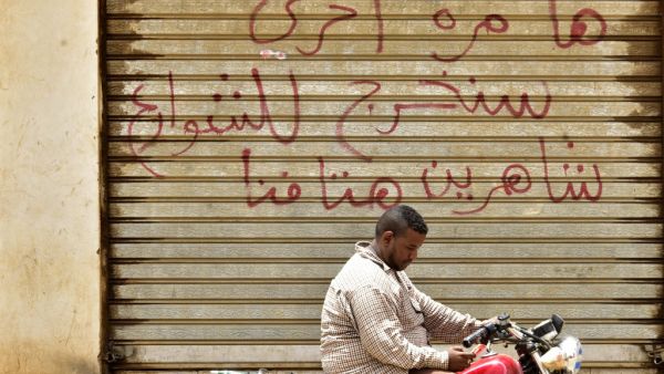 A Sudanese man sits on a motorbike in front of a closed photo studio in Khartoum on June 9, 2019. Arabic writing on the shutters of the closed shop reads: "Another time, we shall take to the streets, crying out our demands loudly." (AFP/ File Photo)