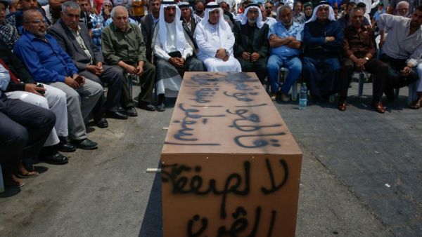 Palestinian men sit around a makeshift coffin with the words "No to the deal of the century", during a protest against a US-led meeting this week in Bahrain on the Palestinian-Israeli conflict, in the village of Yatta near the West Bank city of Hebron, on June 24, 2019. (AFP/ File Photo)