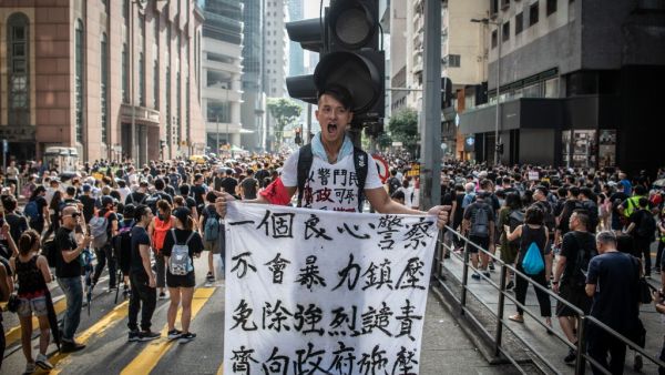 A protester in Wan Chai holds a sign denouncing police violence during a march against a controversial extradition bill in Hong Kong on July 21, 2019. Another huge anti-government march kicked off in Hong Kong on July 21 afternoon with seemingly no end in sight to the turmoil engulfing the finance hub, sparked by years of rising anger over Beijing's rule.  Laurel CHOR / AFP