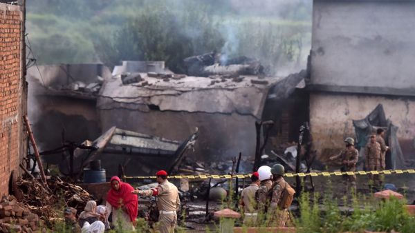 Residents sit among the rubble of their destroyed house as soldiers cordon off the site where a Pakistani Army Aviation Corps aircraft crashed (AFP)