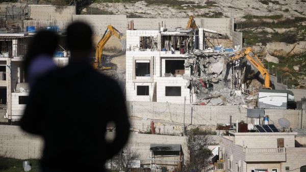 A Palestinian holds a child as he watches Israeli hydraulic shovels demolishing a Palestinian building, north of the occupied West Bank city of Hebron on 14 February 2018 (AFP)