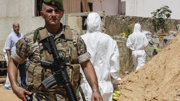 A Lebanese army soldier walks past military intelligence forensic investigators inspecting the scene where two drones came down in the vicinity of a media centre of the Shiite Hezbollah movement  (AFP)