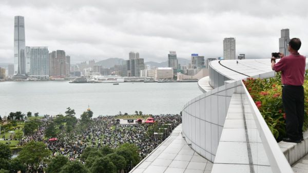 A man takes a photo as protesters gather in Tamar Park to call for a city-wide general strike as they rally against a controversial extradition bill (AFP)