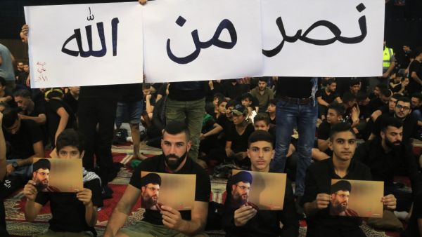 Supporters of the Lebanese Shiite Hezbollah movement hold pictures of the leader Hasan Nasrallah as they watch his speech, transmitted on a large screen in the Lebanese capital Beirut's southern suburbs, on September 2, 2019. (AFP/ File Photo)