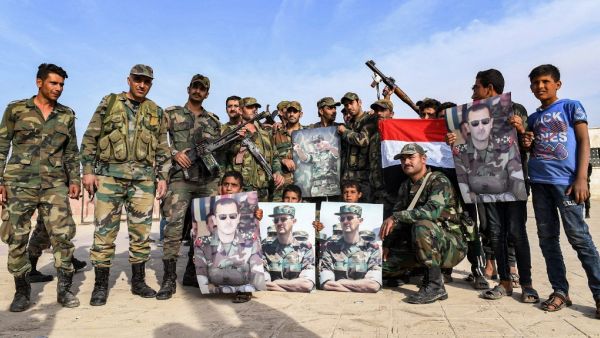 Syrian government soldiers pose for a group photo with a national flag and portraits of President Bashar al-Assad on the outskirts of the northern city of Manbij in the north of Aleppo province as government forces deploy there on October 15, 2019. (AFP/ File Photo)