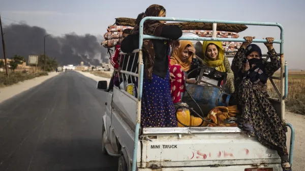 Displaced people, fleeing from the countryside of the Syrian Kurdish town of Ras al-Ain along the border with Turkey, ride in the back of a pickup truck along a road on the outskirts of the nearby town of Tal Tamr on October 16, 2019 as they flee a deadly cross-border Turkish offensive that has sparked an international outcry, with smoke plumes of tire fires billowing in the background to decrease visibility for Turkish warplanes in the area. Delil SOULEIMAN / AFP