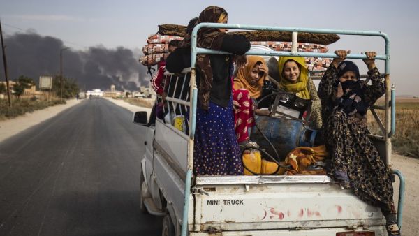Displaced people, fleeing from the countryside of the Syrian Kurdish town of Ras al-Ain along the border with Turkey, ride in the back of a pickup truck along a road on the outskirts of the nearby town of Tal Tamr on October 16, 2019 as they flee a deadly cross-border Turkish offensive that has sparked an international outcry, with smoke plumes of tire fires billowing in the background to decrease visibility for Turkish warplanes in the area. Delil SOULEIMAN / AFP