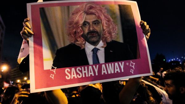 A Lebanese protester lifts a picture of Prime Minister Saad Hariri in a wig during a rally in downtown Beirut on the third day of demonstrations against tax increases and official corruption, on October 19, 2019. The writing "sashay away" refers to a catchphrase from a drag queen TV show meaning "leave". IBRAHIM AMRO / AFP