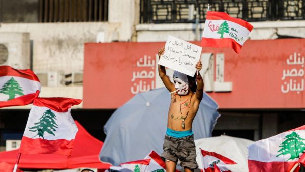 A topless Lebanese boy wearing body paint coloured with the Lebanese national flag and reading in Arabic "revolution" holds up a sign protesting against the ruling elites as others wave national flags during a demonstration on the sixth day of protest against tax increases and official corruption, at Nur Square in Lebanon's northern port city of Tripoli, on October 22, 2019. (AFP/ File Photo)
