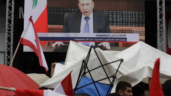 Lebanese people take cover from the rain under umbrellas as they watch a televised speech by President Michel Aoun, during a demonstration on the eighth day of protest against tax increases and official corruption, in Zouk Mosbeh, north of the capital Beirut, on October 24, 2019. The Lebanese president broke his silence after a week of unprecedented protests and expressed willingness to meet the demonstrators. JOSEPH EID / AFP