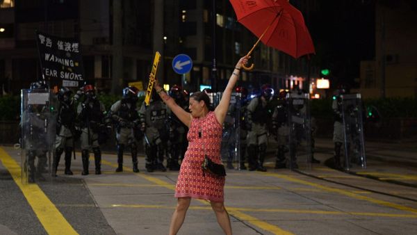 A woman holds up an umbrella and license plates, one that reads 'angel', as she stands in front of a row of riot police during violent clashes with demonstrators in the Causeway Bay district of Hong Kong on October 1, 2019. (AFP/ File Photo)