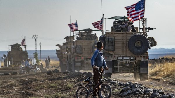 A Syrian boy on his bicycle looks at a convoy of US armoured vehicles patrolling fields near the northeastern town of Qahtaniyah at the border with Turkey, on October 31, 2019. US forces accompanied by Kurdish fighters of the Syrian Democratic Forces (SDF) patrolled part of Syria's border with Turkey, in the first such move since Washington withdrew troops from the area earlier this month, an AFP correspondent reported. Delil SOULEIMAN / AFP