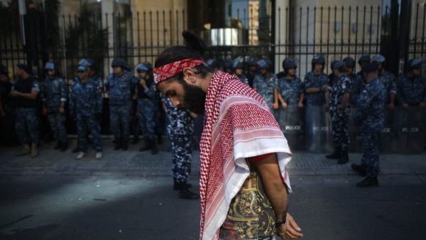 A Lebanese protester draped in a traditional Palestinian Keffiyeh scarf walks past a row of security forces during ongoing anti-government demonstrations in central Beirut  (AFP)