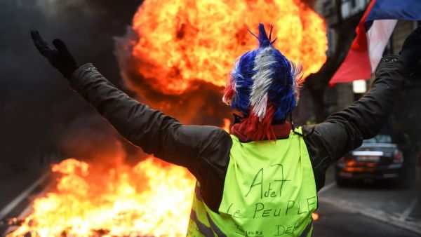 In this file photo taken on December 29, 2018 A "Yellow vest" (gilets jaunes) anti-government demonstrator holds up the French flag as he stands infront of a fire during protests in the western French city of Bordeaux. On November 17, 2018, 282,000 people according to the authorities, responded to a Facebook call, yellow vest on their backs, outside any political or trade union framework, and invested hundreds of roundabouts, symbols of the peri-urban France. The movement, born after a contested planned fue
