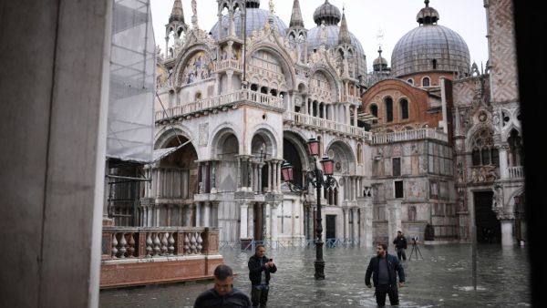 People wearing thigh boots cross flooded St. Mark's square by St. Mark's Basilica after an exceptional overnight "Alta Acqua" high tide water level Marco Bertorello / AFP