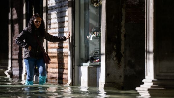 A woman carefully walks across a flooded arcade on November 14, 2019 in Venice. Much of Venice was left under water after the highest tide in 50 years ripped through the historic Italian city, beaching gondolas, trashing hotels and sending tourists fleeing through rapidly rising waters. Filippo MONTEFORTE / AFP