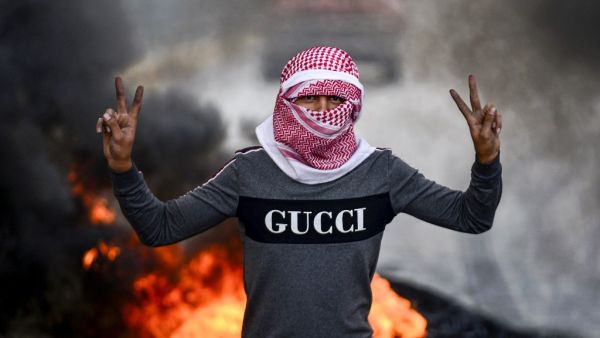 A masked Iraqi protester flashes the victory gesture as he stands before burning tires at a roadblock in the central holy shrine city of Najaf on November 18, 2019. (Haidar HAMDANI / AFP)