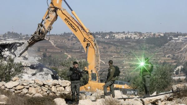 An Israeli border guard points a laser light at the camera as others keep watch while a bulldozer demolishes Palestinian houses near al-Arub camp, on the outskirts of the West Bank town of Hebron (AFP)