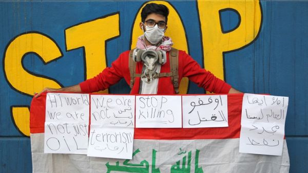 An 18-year-old Iraqi student wearing a surgical mask and a gas mask around his neck poses for a picture while holding up a national flag covered with messages in English and Arabic, during an anti-government demonstration in the capital Baghdad on November 21, 2019.  (AFP/ File Photo)