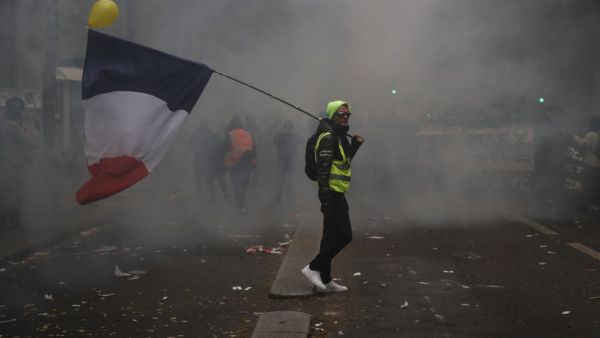 A man holding a French flag and a yellow vest walks in tear gas during a demonstration against the pension overhauls, in Paris, on December 5, 2019 as part of a nationwide strike. Trains cancelled, schools closed: France scrambled to make contingency plans on for a huge strike against pension overhauls that poses one of the biggest challenges yet to French President's sweeping reform drive. Zakaria ABDELKAFI / AFP